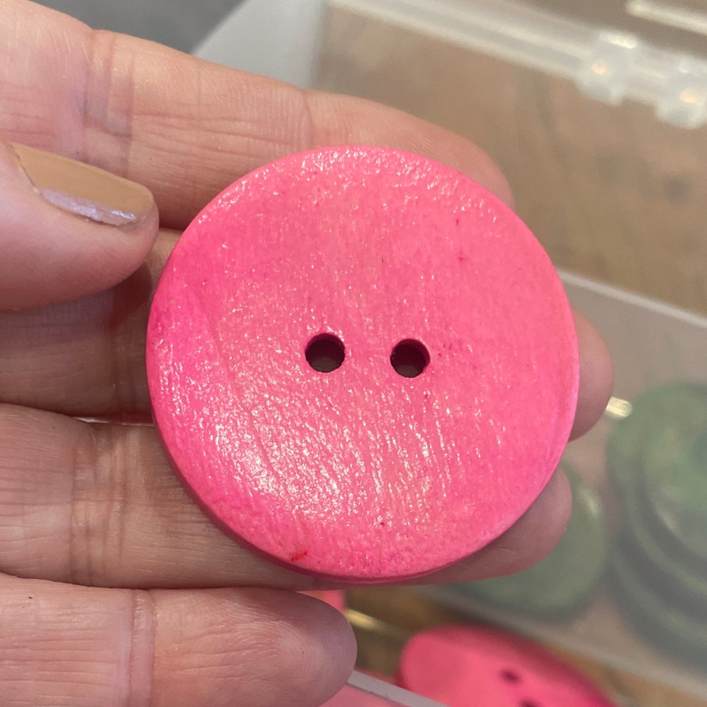 Pink button held by a hand with a container of buttons in the background
