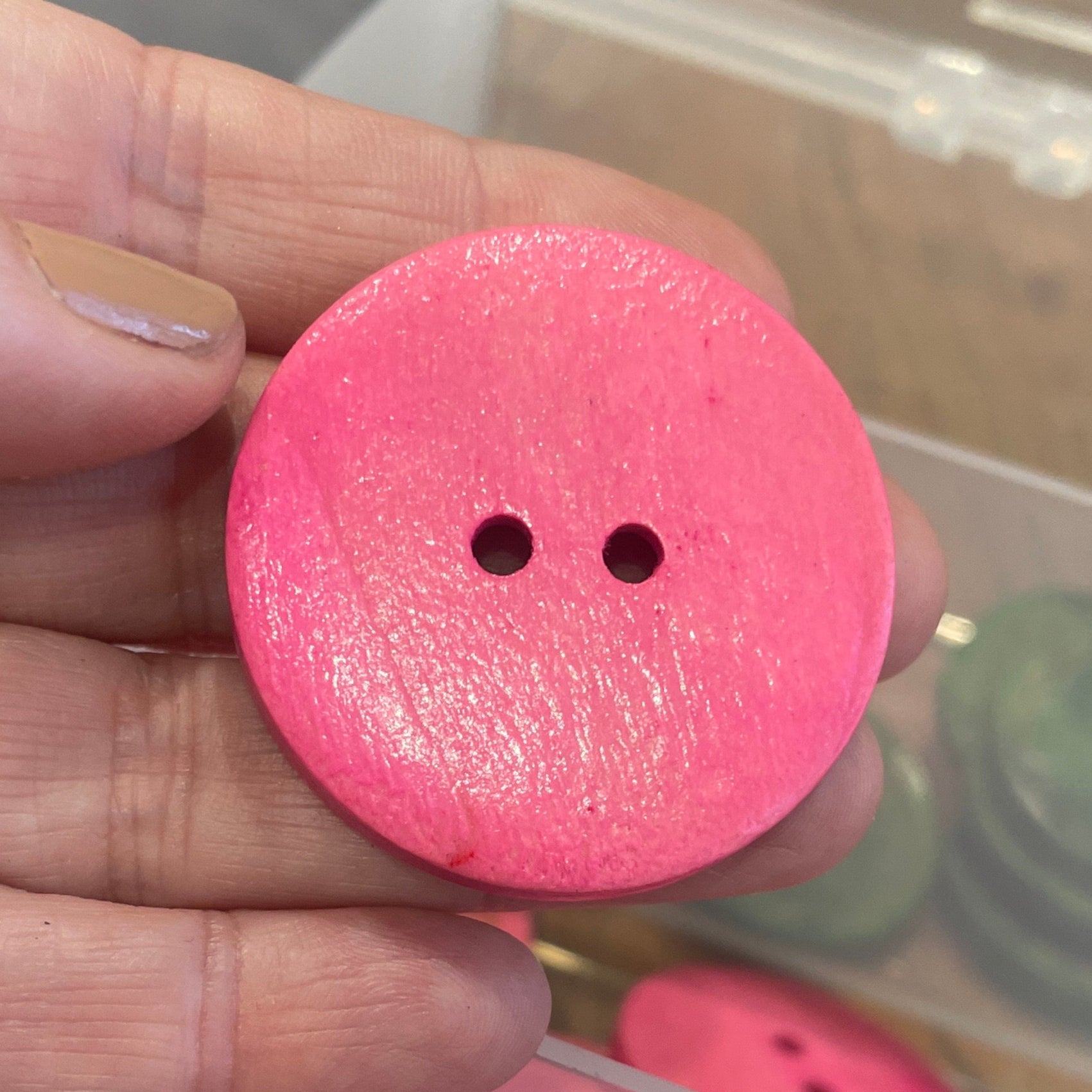 Pink button held by a hand with a container of buttons in the background