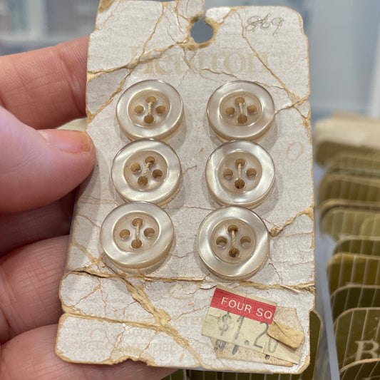 Hand holding a decorative buttons, surrounded by similar items in the background.