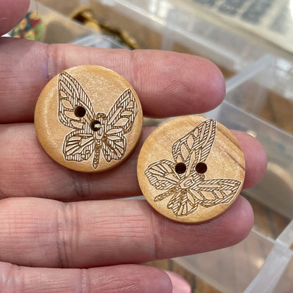 Wooden buttons with butterfly design held in hand, with a container of assorted buttons in the background.