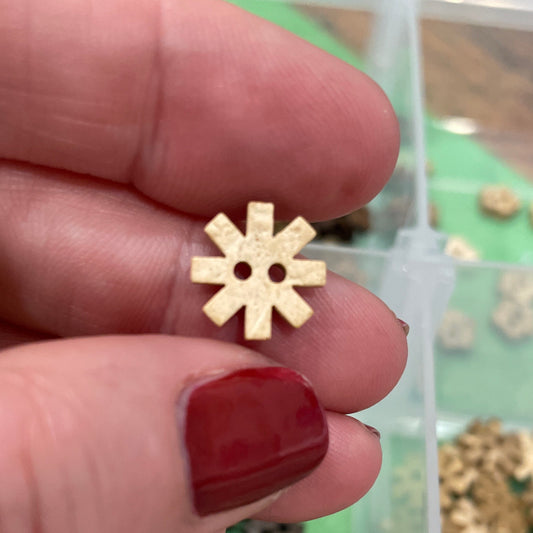 Gold gear-shaped button  held between fingers with a container of buttons in the background