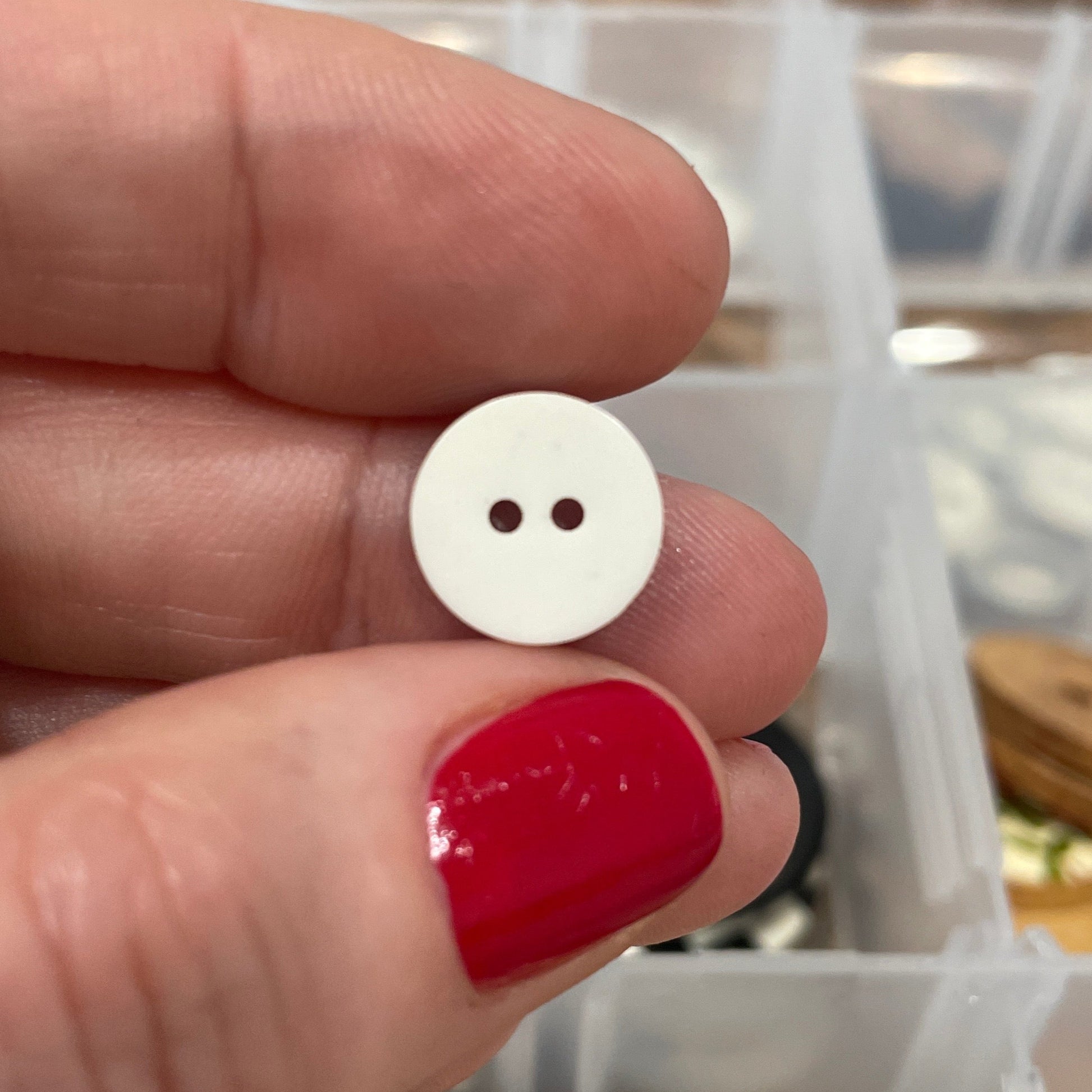 Hand holding a white button with a blurred background of button collection