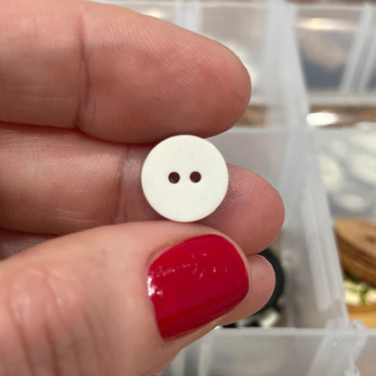 Hand holding a white button with a blurred background of button collection
