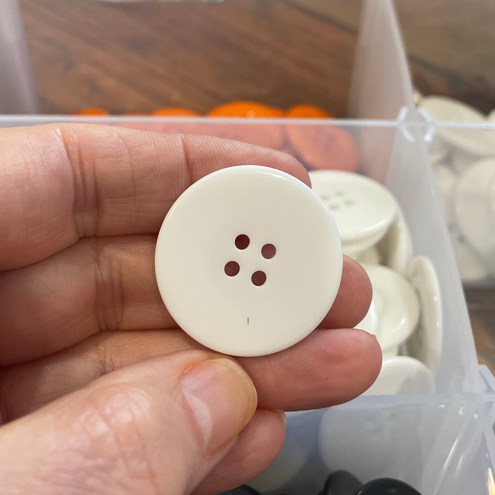 Hand holding a white button with a blurred background of buttons and a clear container.