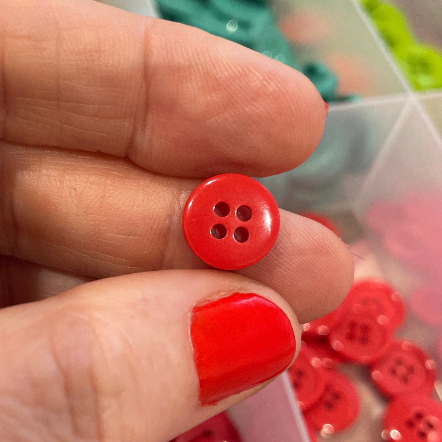 Red button held between fingers with a container of buttons in the background