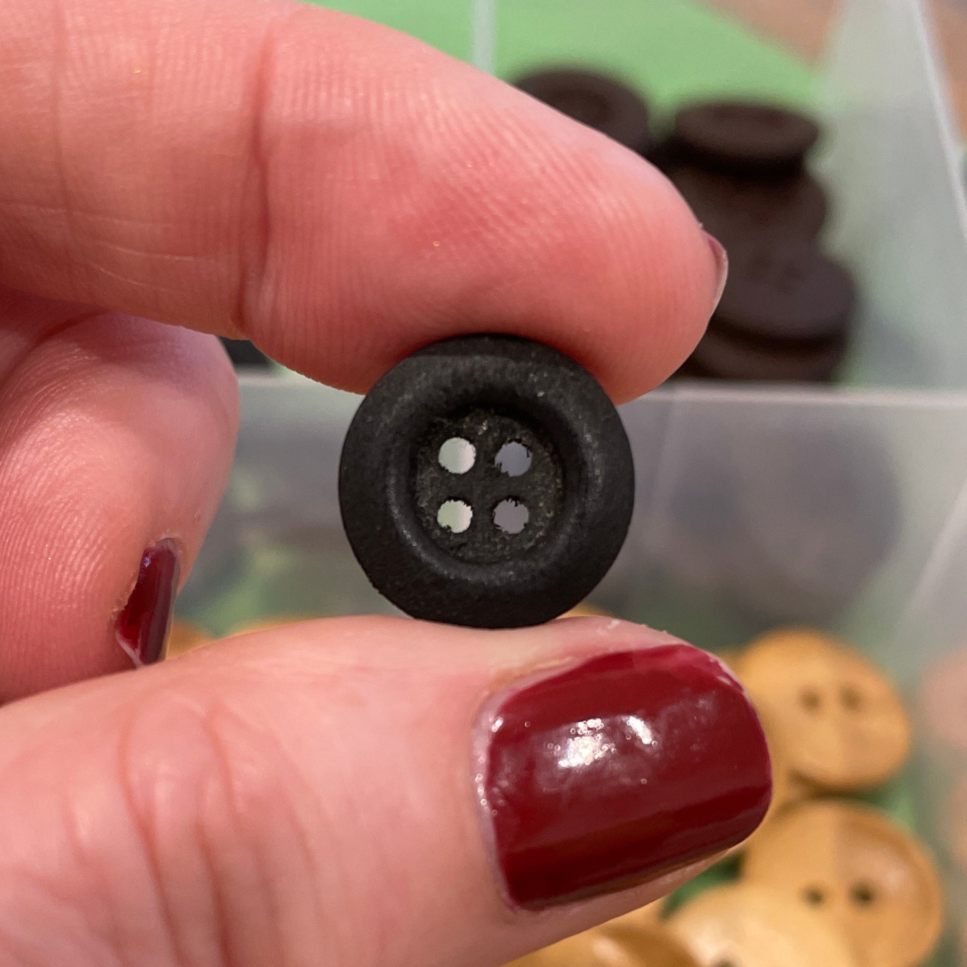 Hand holding a black button with a container of buttons in the background