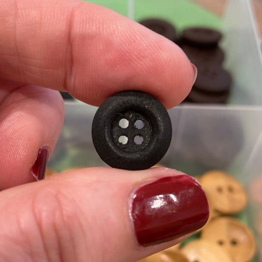 Hand holding a black button with a container of buttons in the background