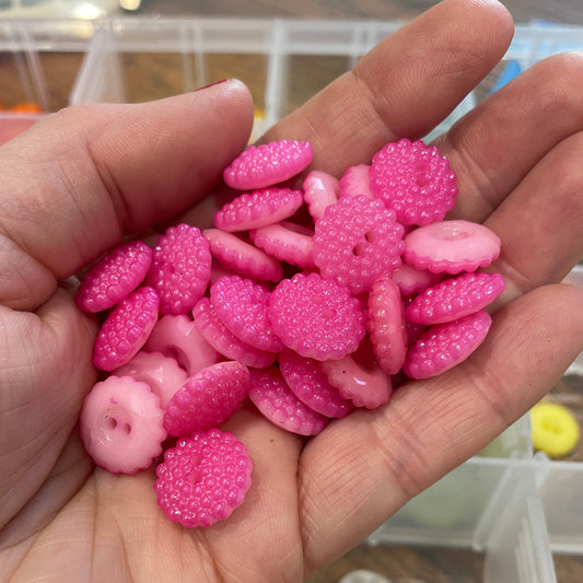 Hand holding pink buttons with a background of button containers.