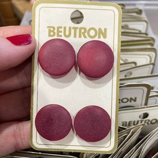 Four maroon circular buttons on a Beutron branded card held by a hand.