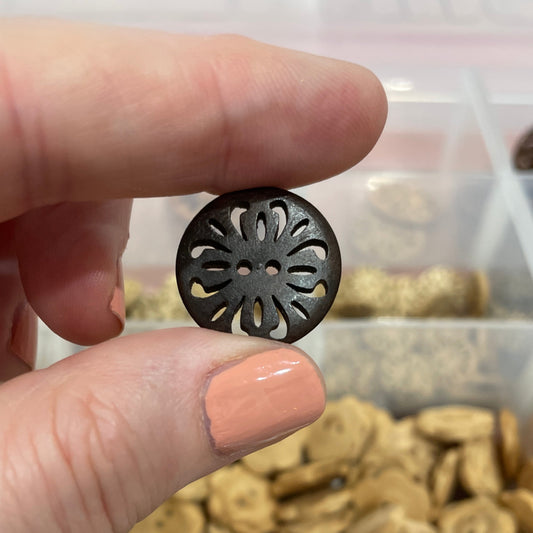Hand holding a decorative button with a container of assorted buttons in the background