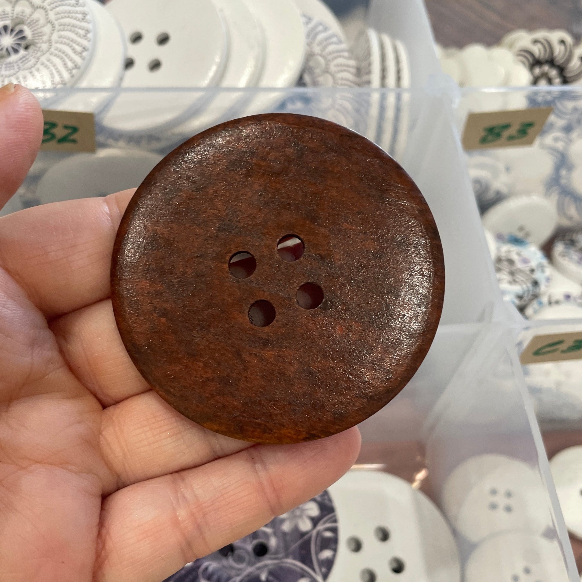 Brown button held by a hand with a container of various buttons in the background