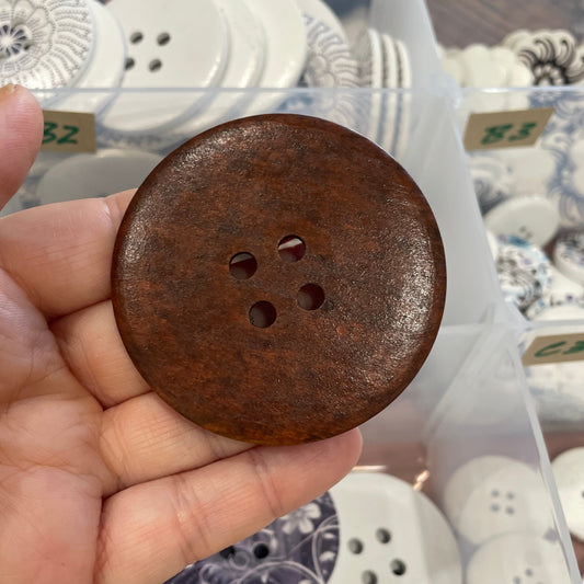 Brown button held by a hand with a container of various buttons in the background