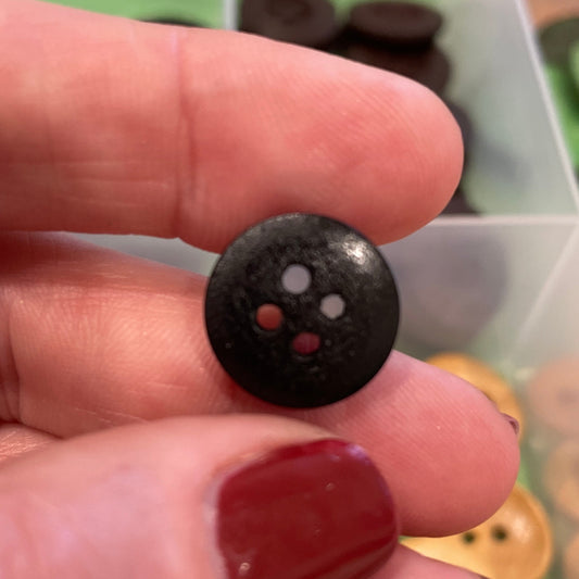 Black button held between fingers with a container of buttons in the background