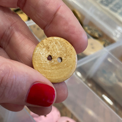 Hand holding a gold button with a clear container of assorted buttons in the background