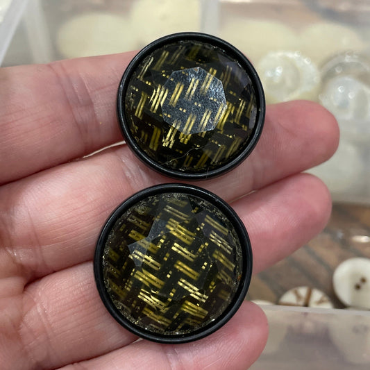 Two black and gold circular objects held in a hand with a blurred background of beads.