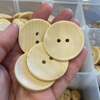 Hand holding three wooden buttons with a blurred background of more buttons and containers.