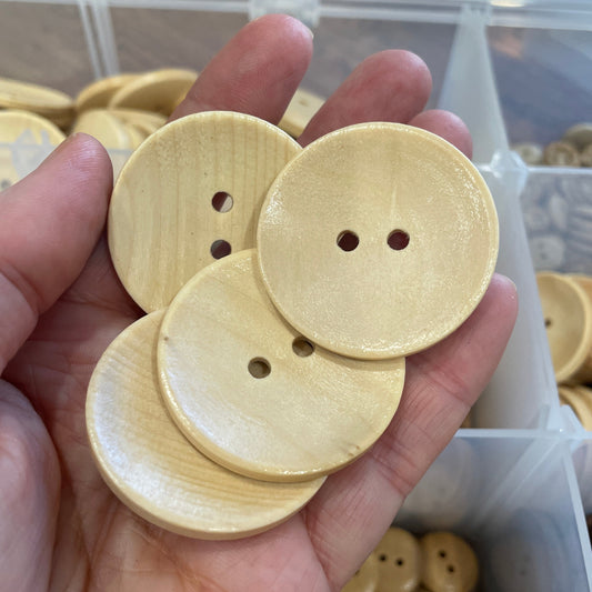 Hand holding three wooden buttons with a blurred background of more buttons and containers.