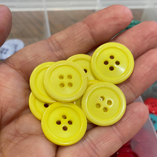 Hand holding yellow buttons with a container of red and blue buttons in the background