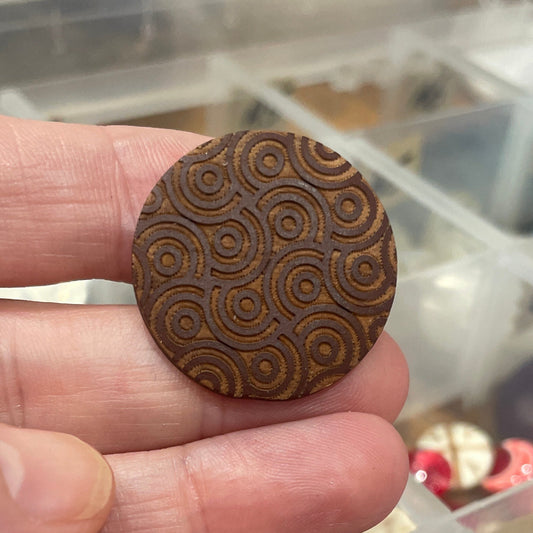Wooden button held between fingers with a container of buttons in the background