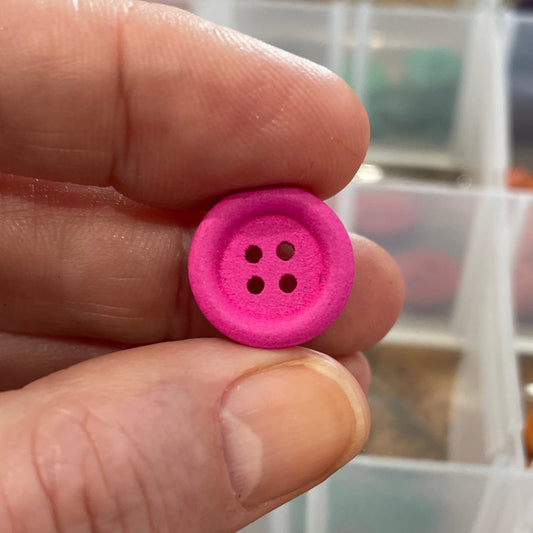 Hand holding a pink button with a container of assorted buttons in the background