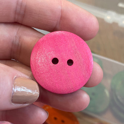 Pink button held by a hand with a container of buttons in the background