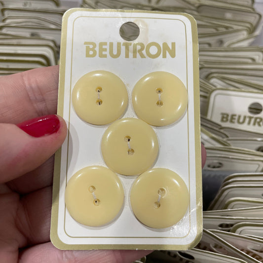 Pack of beige buttons with 'BEUTRON' branding held by a hand.