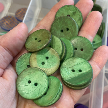 Hand holding green buttons with a background of button containers.