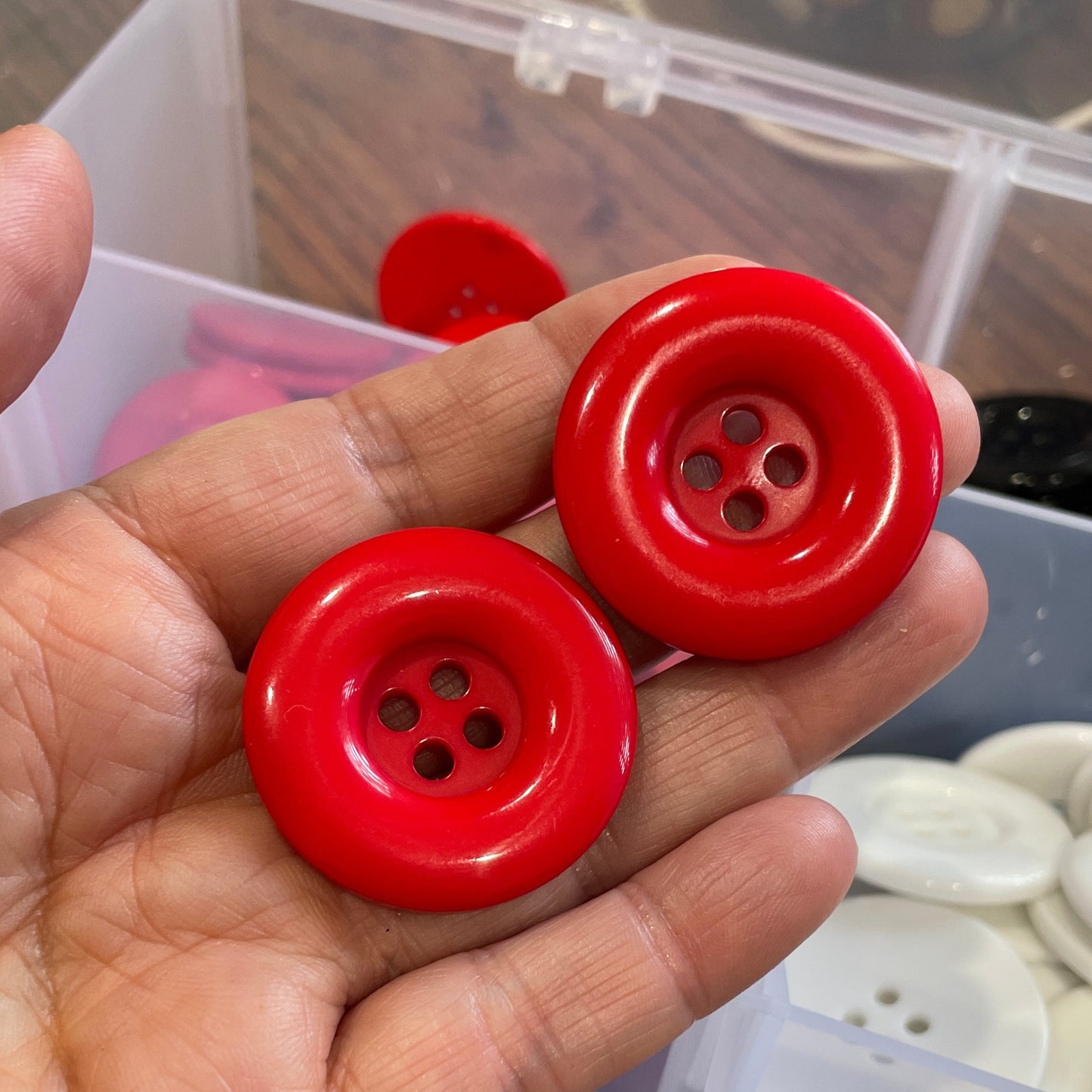Hand holding two red buttons with a container of buttons in the background