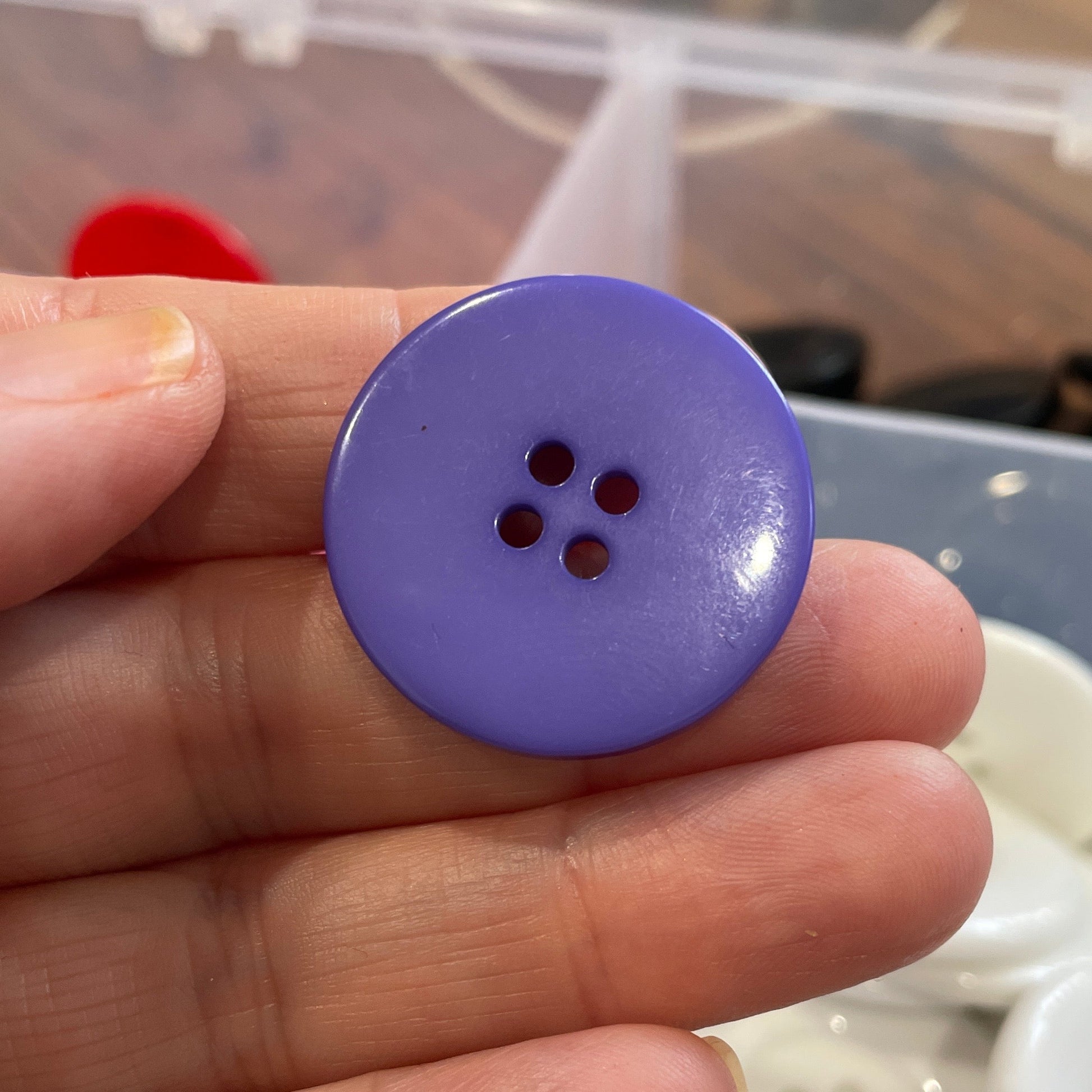 Hand holding a purple button with a blurred background of buttons and fabric.