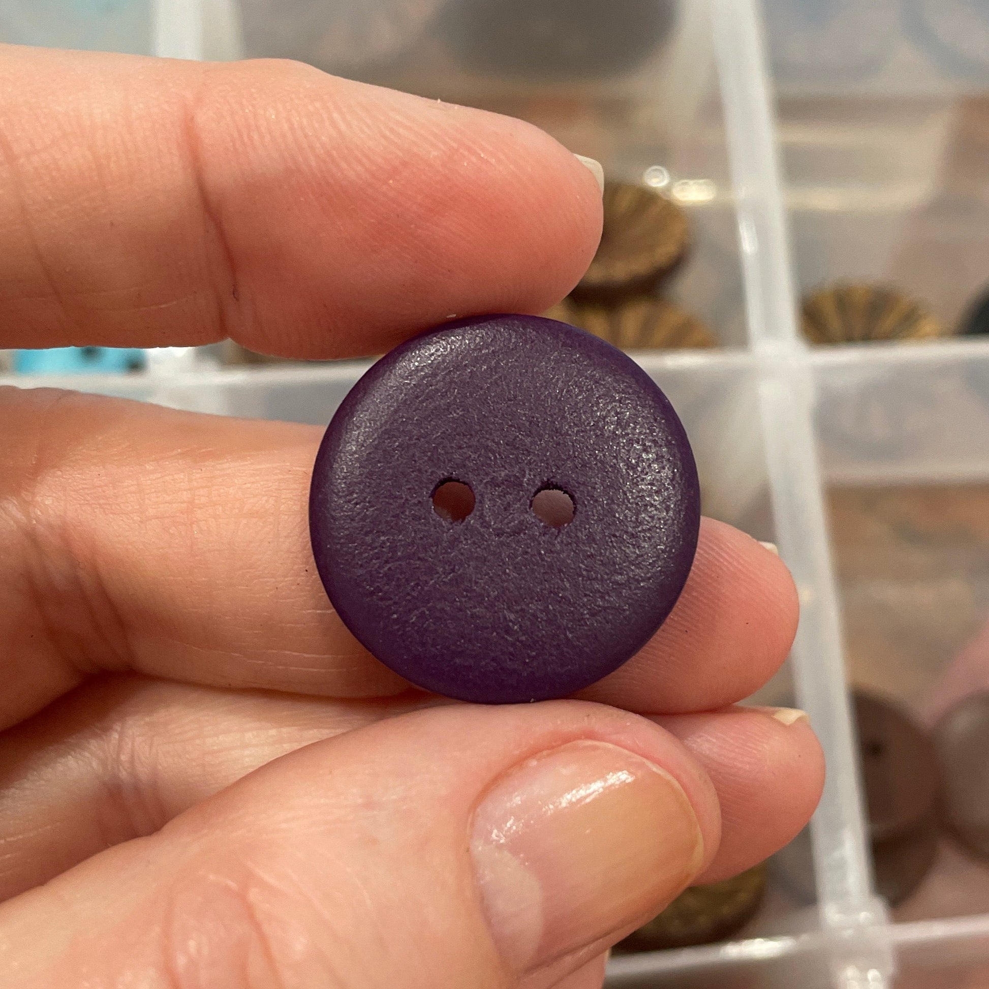 Hand holding a purple button with a clear container of assorted buttons in the background