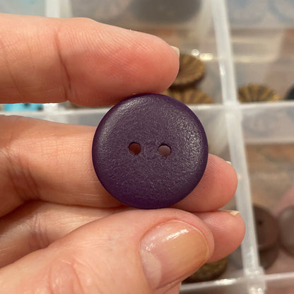 Hand holding a purple button with a clear container of assorted buttons in the background