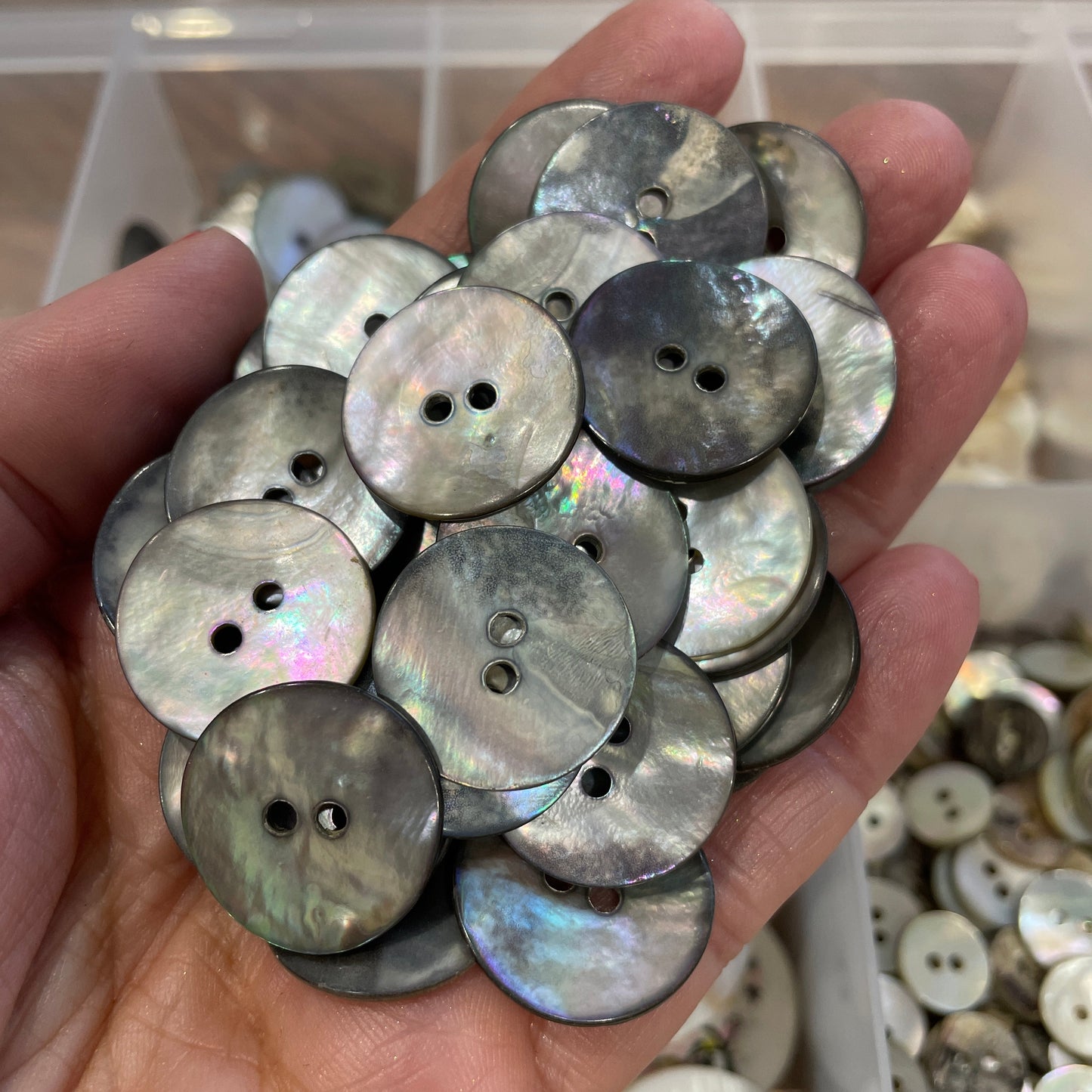 Hand holding a collection of round, metallic buttons with a blurred background of more buttons.