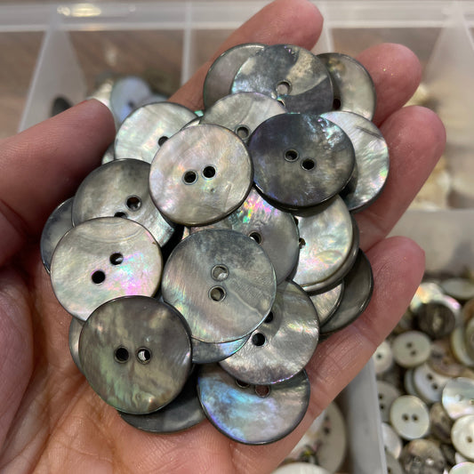 Hand holding a collection of round, metallic buttons with a blurred background of more buttons.