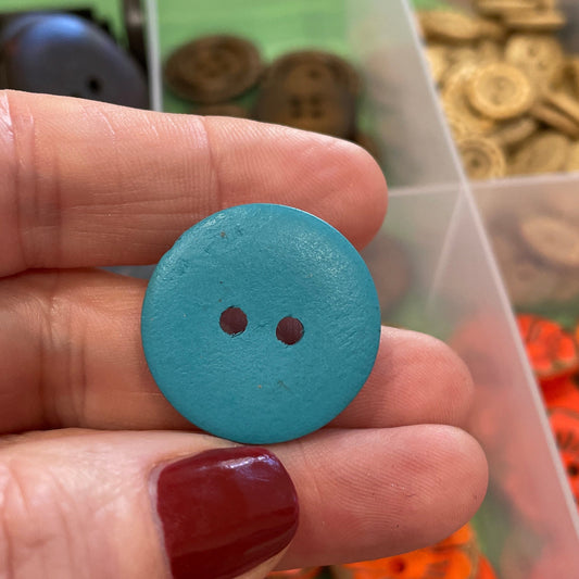 Hand holding a blue button with a collection of buttons in the background