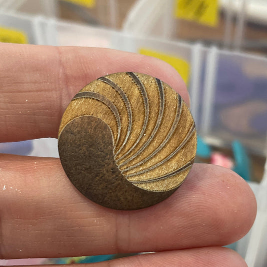 Close-up of a hand holding a wooden button with a pattern, with a background of button assortments.