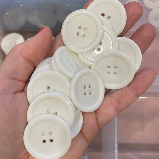 Hand holding white buttons with a clear container of black buttons in the background
