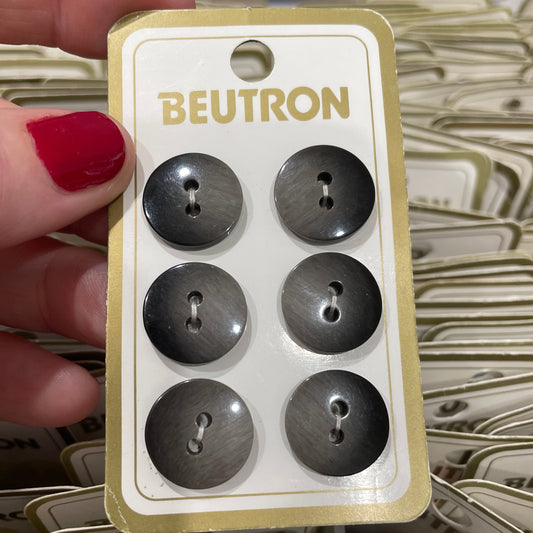 Set of six gray buttons on a BEUTRON branded card held by a hand with red nail polish.