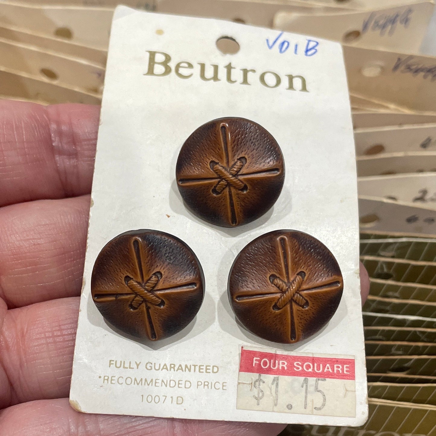 Hand holding a package of brown buttons with a Beutron label.