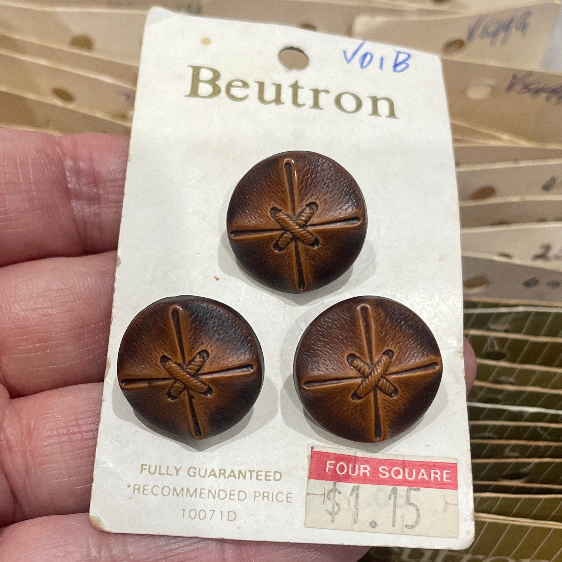 Hand holding a package of brown buttons with a Beutron label.