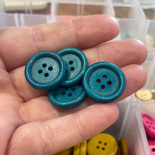 Hand holding blue buttons with a container of colorful buttons in the background.