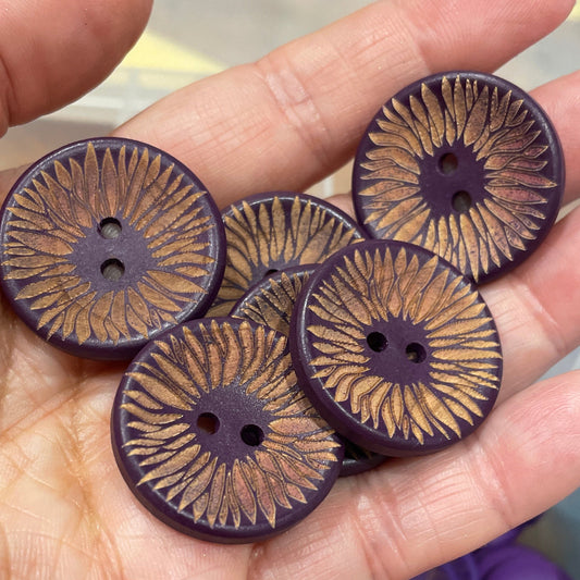 Hand holding purple decorative buttons with a container of buttons in the background