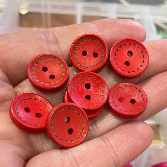 Red buttons held in a hand with a container of pink buttons in the background