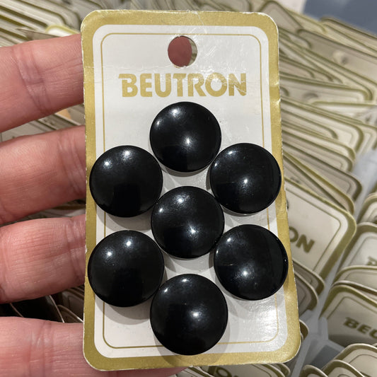 Black round buttons on a BEUTRON card held by a hand with more cards in the background.