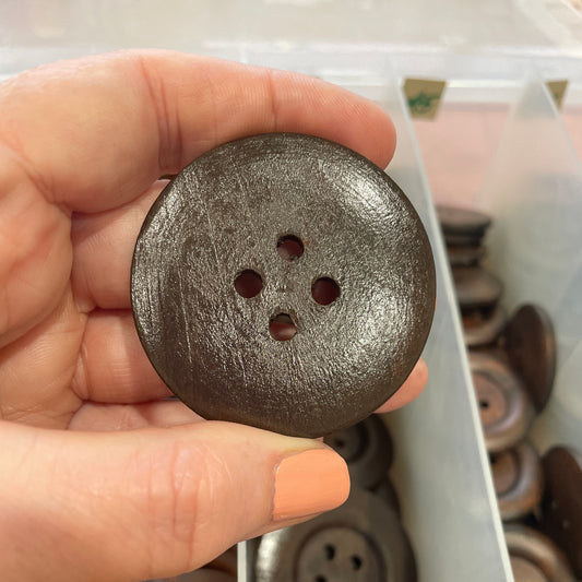 Hand holding a large metallic button with a blurred background of more buttons.