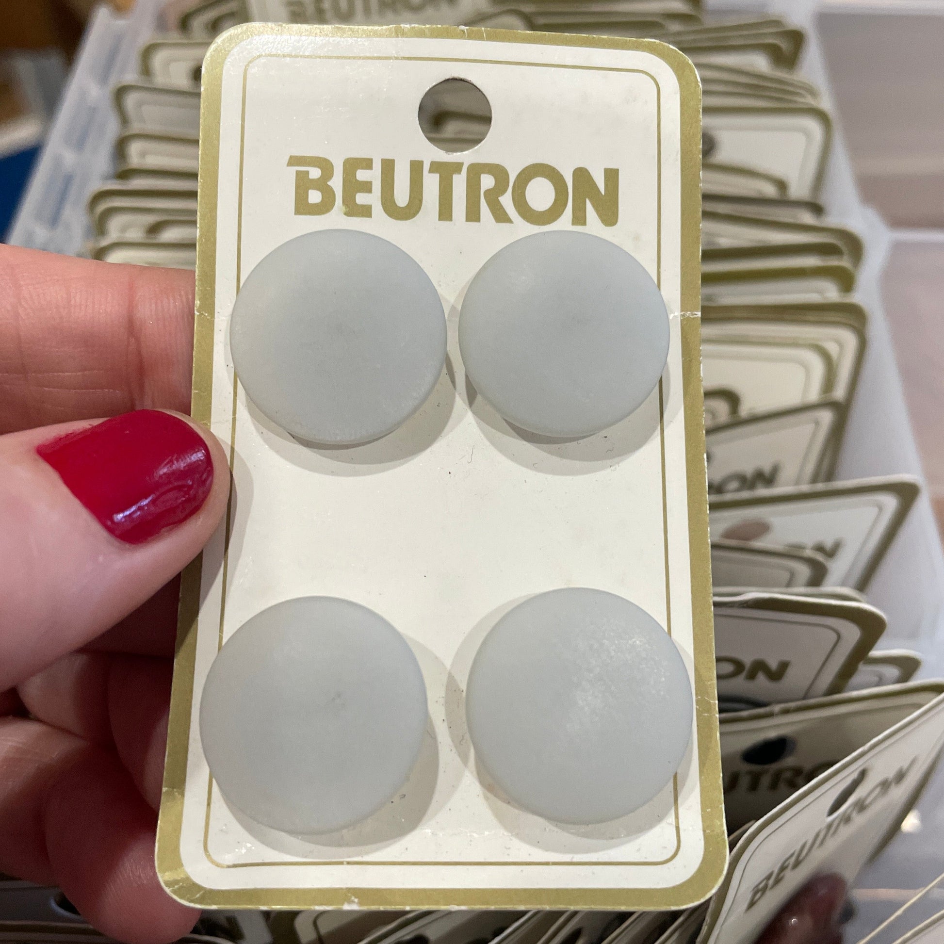 Pack of BEUTRON buttons  held by a hand with red nail polish, surrounded by similar packaging.