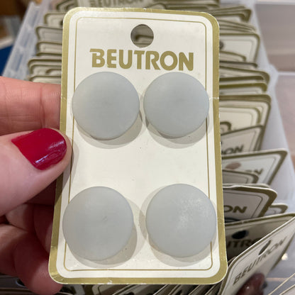 Pack of BEUTRON buttons  held by a hand with red nail polish, surrounded by similar packaging.