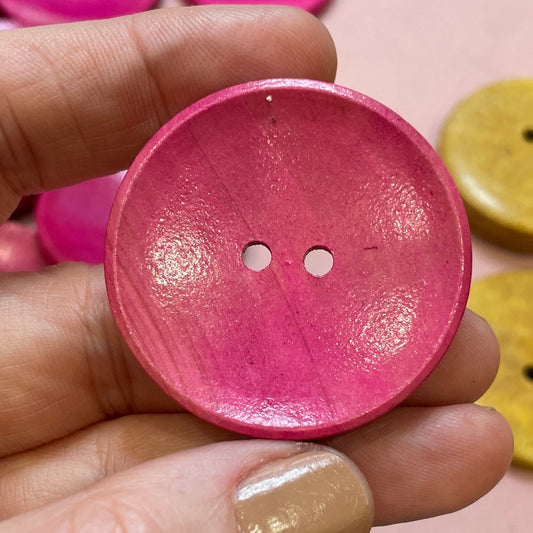 Hand holding a pink button with colorful buttons in the background