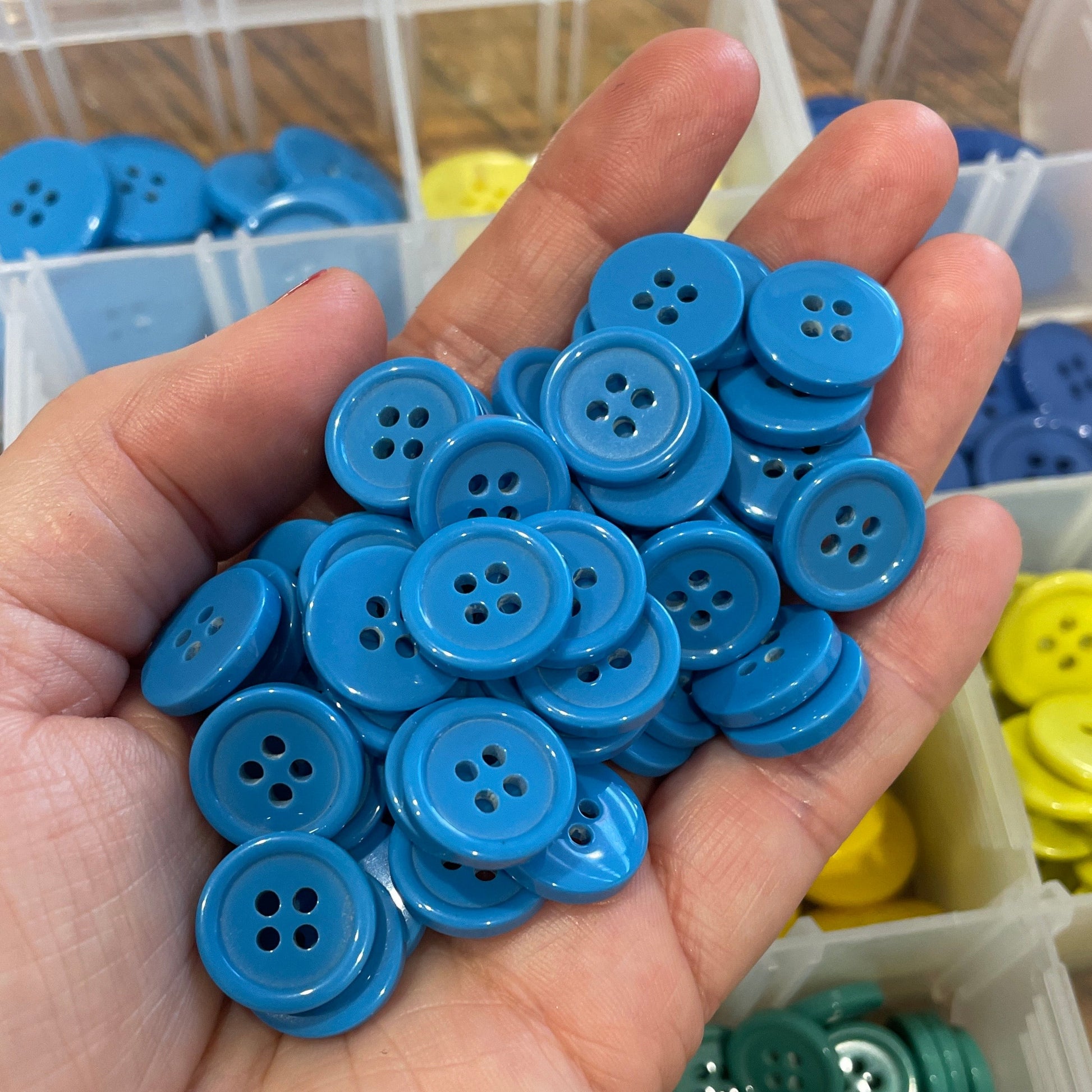 Hand holding blue buttons with containers of buttons in the background