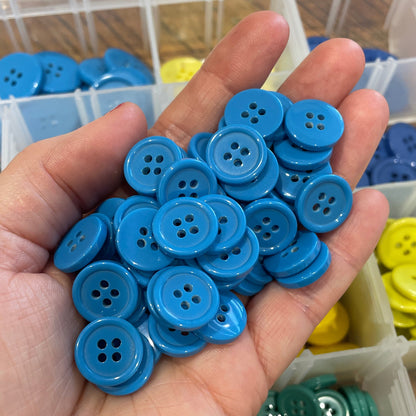 Hand holding blue buttons with containers of buttons in the background