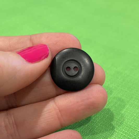 Black button held between fingers against a green background